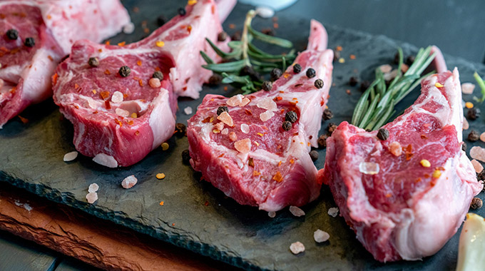 Lamb chops being seasoned with rock salt and herbs