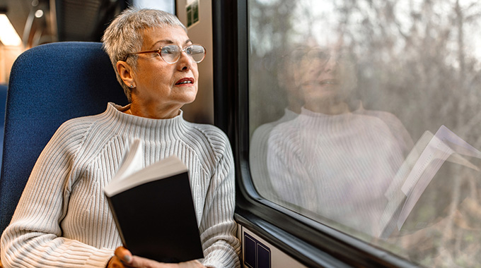 A woman holding a book looks out a train window.