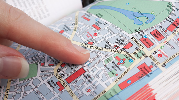 A finger points at an intersection on a paper map of London