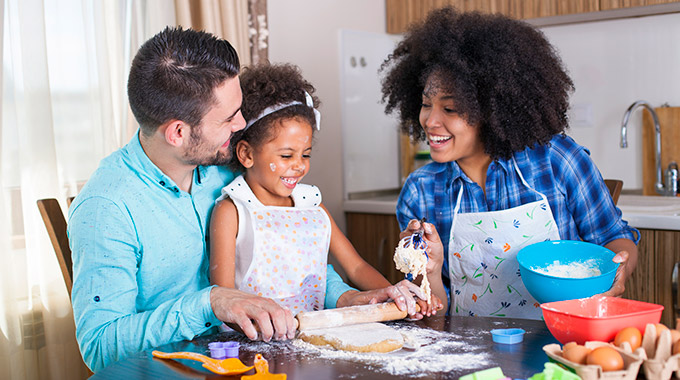 A mother and father bake with their young child in the kitchen