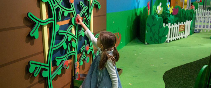 Girl placing fake apples on wall at Peppa Pig's World of Play. Girl placing fake apples on wall at Peppa Pig's World of Play.
