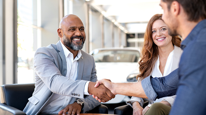 Men at car dealership shaking hands.