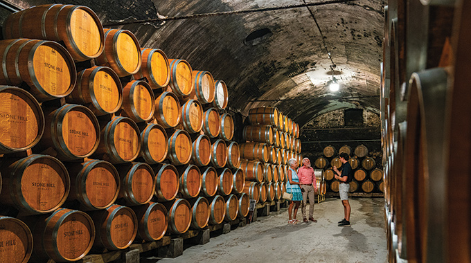 Couple and tour guide surrounded by wine barrels in the Stone Hill Winery cellar.