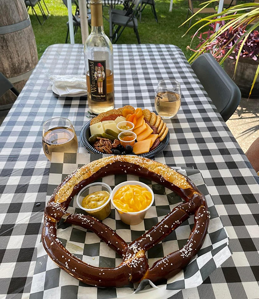 Large German-style pretzel served alongside a charcuterie platter and wine.