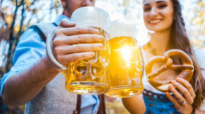 A couple holding a soft pretzel and steins of beer