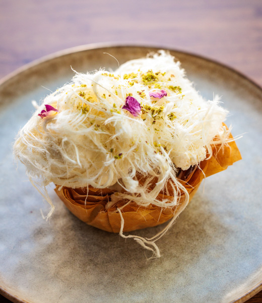 Pastry bowl filled with ice cream and dates covered in cotton candy and crushed pistachios.
