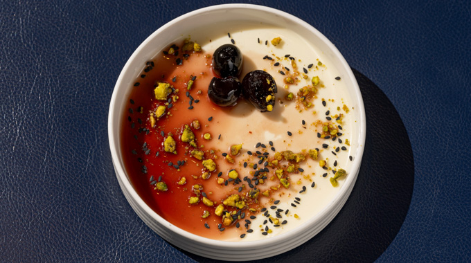 Panna cotta topped with cream, cherries, pistachio crumble, and black sesame seeds.