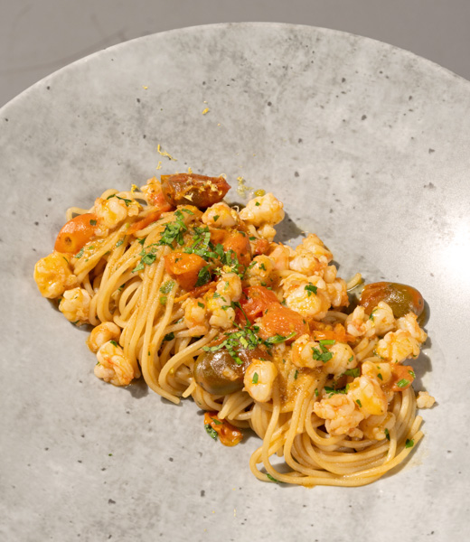 Spaghetti topped with shrimp and tomatoes.