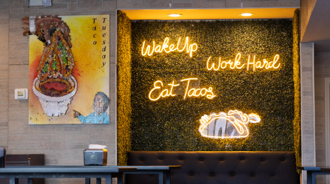 Neon sign inside TJ Birria y Mas that says "wake up, work hard, eat tacos."