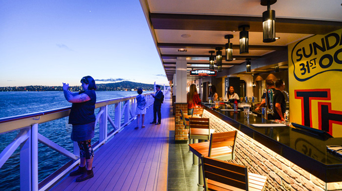 Woman standing by cruise ship bar photographing the ocean view with her phone