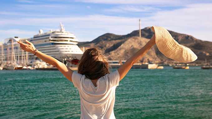 Person holding up a sun hat while looking toward a cruise ship