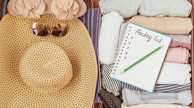 Suitcase with a sun hat, sunglasses, sandals, clothes, and a notebook open to a page with the words "packing list"