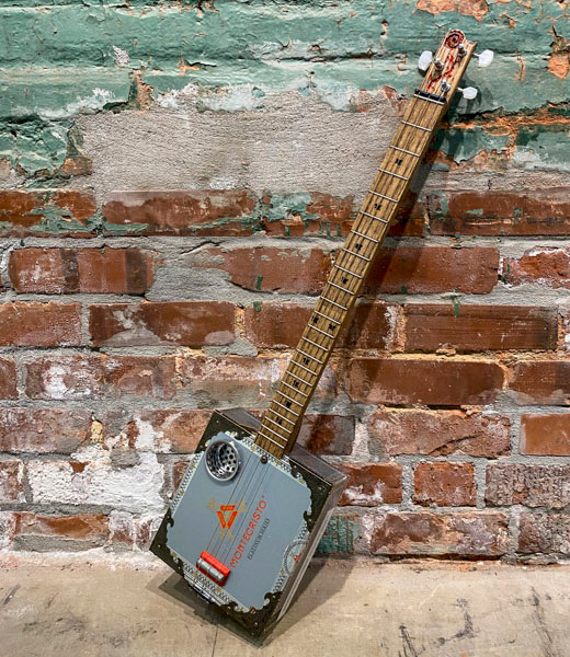 A handmade cigar box guitar leaned against a brick wall.