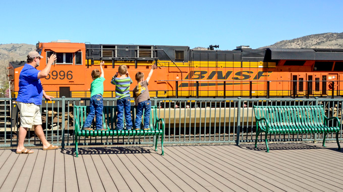 A man and 3 young boys waving at a passing train.