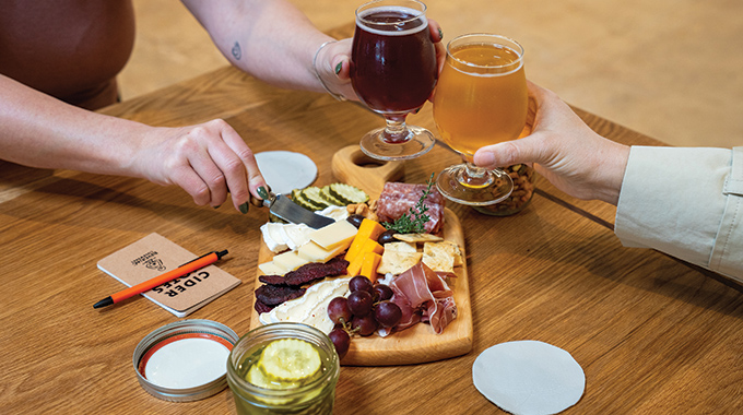 Guests toasting glasses of cider over a charcuterie board.