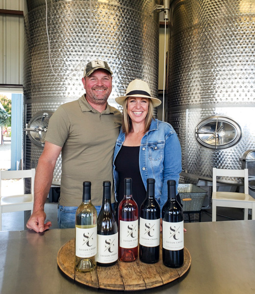 Brian and Katie Babcock with various wine bottles inside their tasting room.