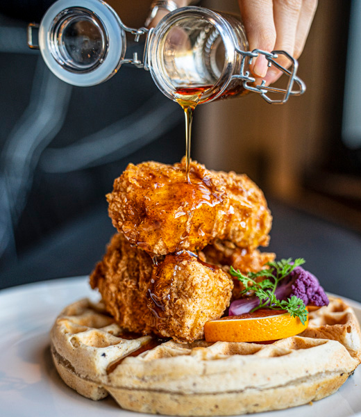 Syrup being poured onto fried chicken served over a waffle.