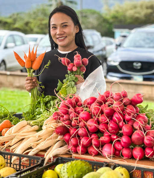 Woman holding up fresh carrots and raddishes