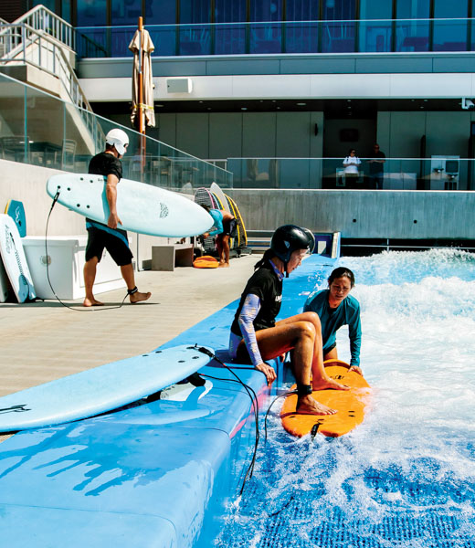 Author Mindy Pennybacker seated at the edge of the wave pool as an instructor holds her board.