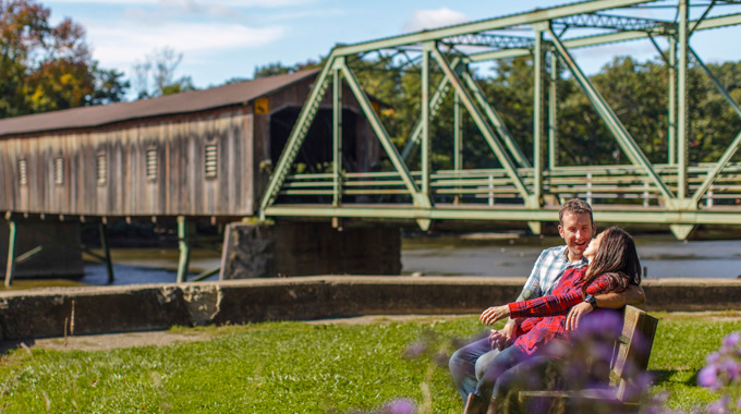 Couple relaxing on a bench, with the Harpersfield Covered Bridge in the background