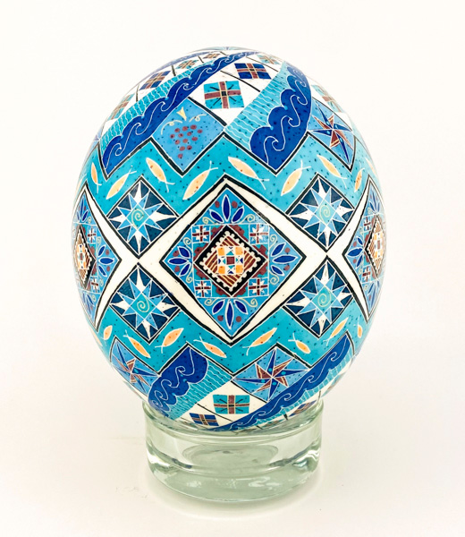 Pysanka ostrich egg decorated with waves, fish, grapes, and other motifs.