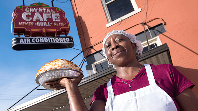 Employee holding up a meringue pie, the Crystal Grill sign in the background.