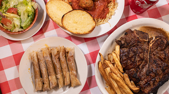 Spread of food at Doe’s Eat Place including tamales, steak, spaghetti, and salad.