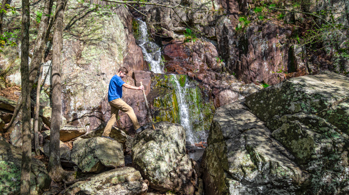 Hiker using a walking stick to reach Mina Sauk Falls.